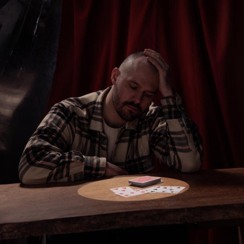 Andrew looks introspectively down at a table where a deck of cards is lit by a spotlight.