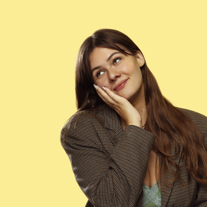 Alex looking content resting their hand on their hands against a butter yellow background.