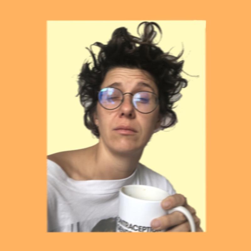 Photo of performer with bed head hair, skewed glasses and holding a mug.