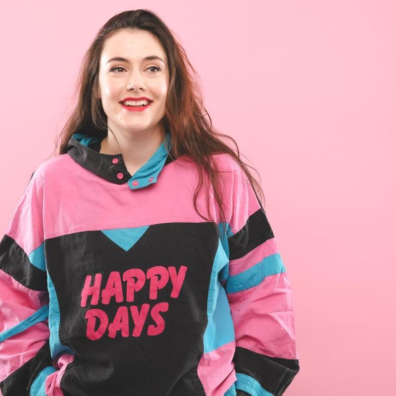 Marjolein in front of a pink background wearing a top that says happy days