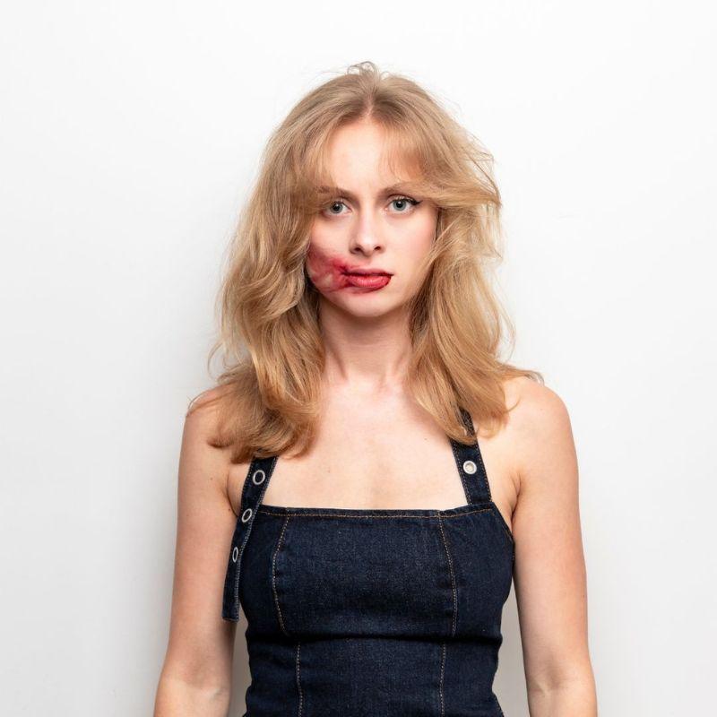 Olivia facing the camera straight faced with red lipstick smudged across their face