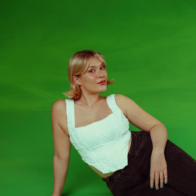 Cecily posing in a white corset style top with a dark green background.