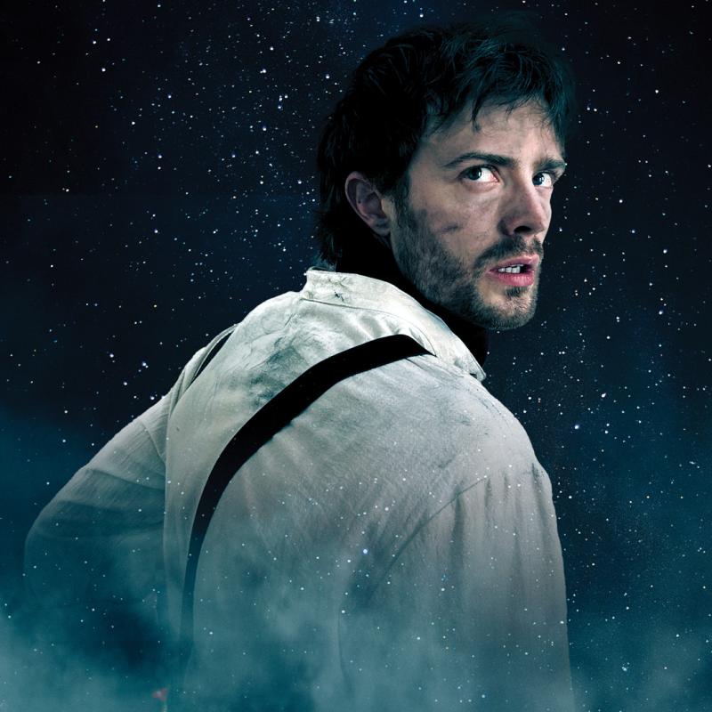 A Man stares into the distance, below him the Titanic sinks into the ocean with smoke and ice visible. 