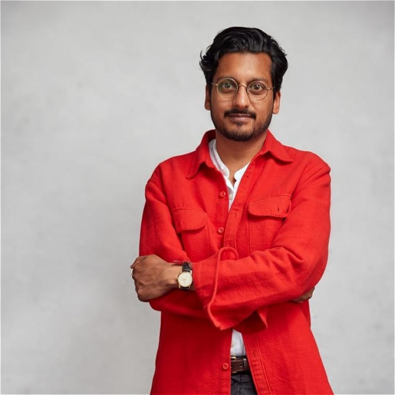 Photo of performer with arms loosely folded wearing an orange over shirt.