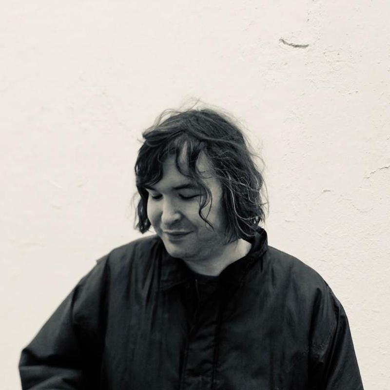 Monochrome headshot of Johnny against a white wall looking down.