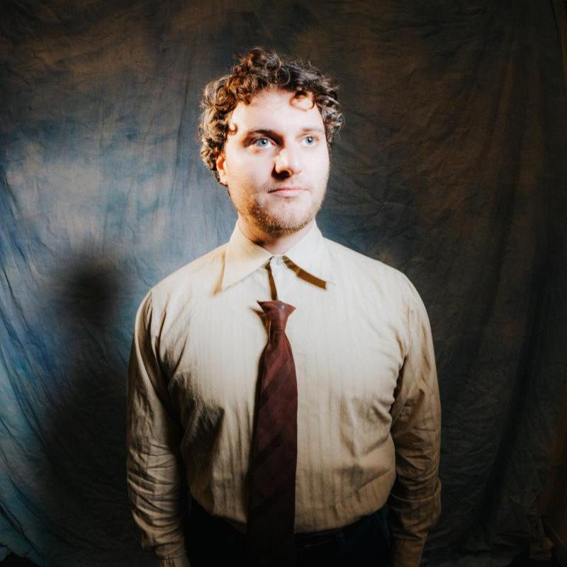 Photo of Jonathan in a brown shirt and tie.