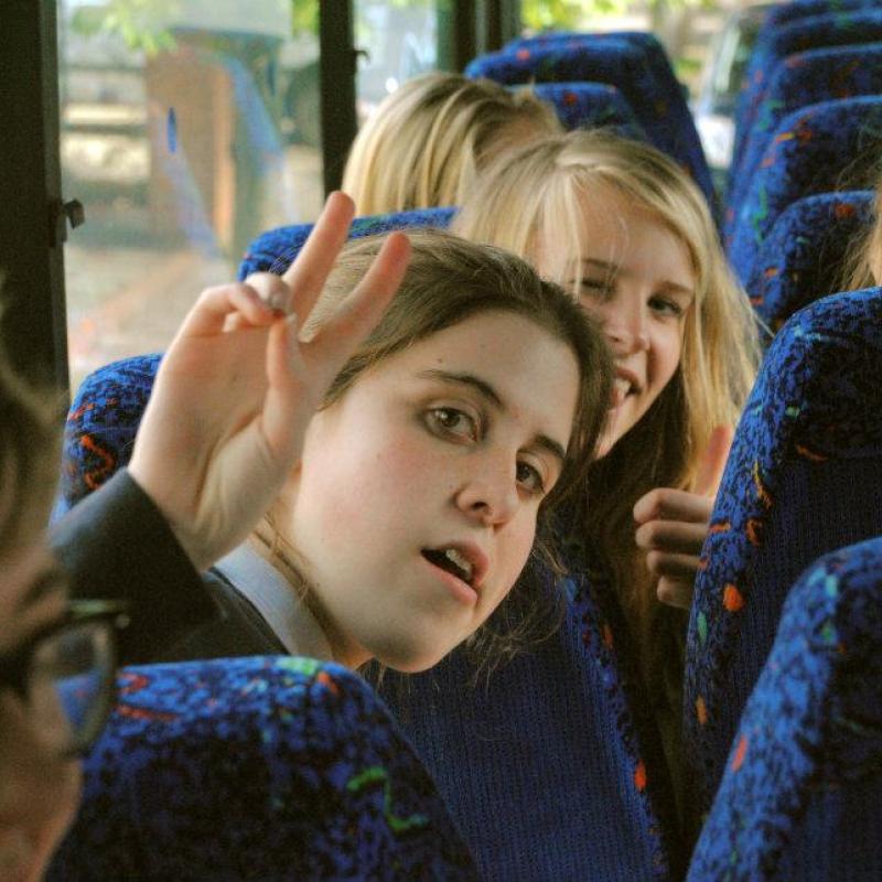 Photo of Ele as a school child on the bus giving the peace sign.