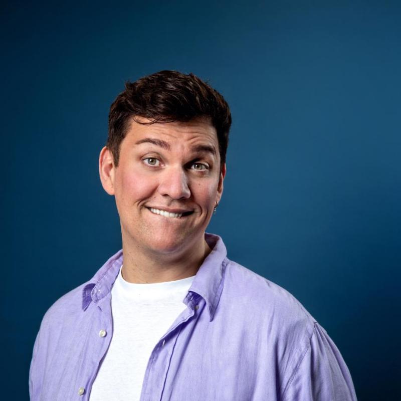 Dane grinning cheekily at the camera with a plain blue backdrop