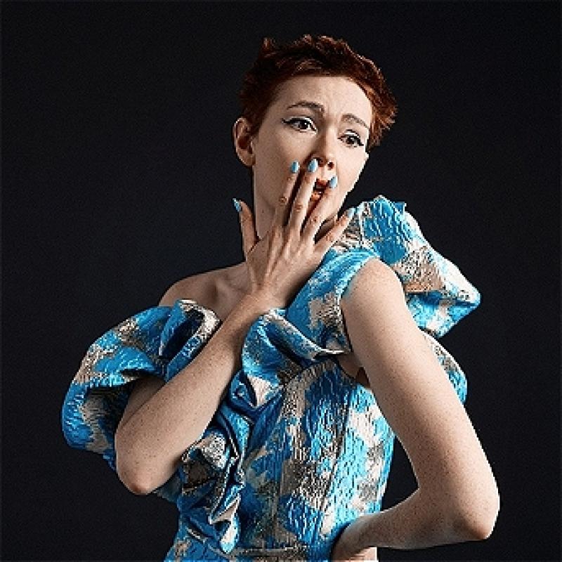 Elf stands majestic and feigning surprise in a fashionable blue and white dress 