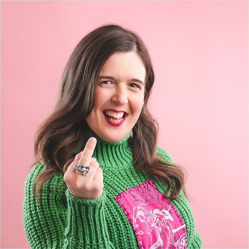 Photo of a smiling Rosie Jones swearing and sticking their middle finger up.