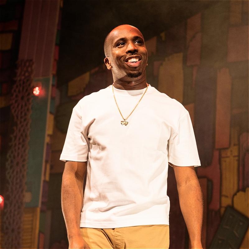 Kiell stands with a white shirt and chain smiling off camera