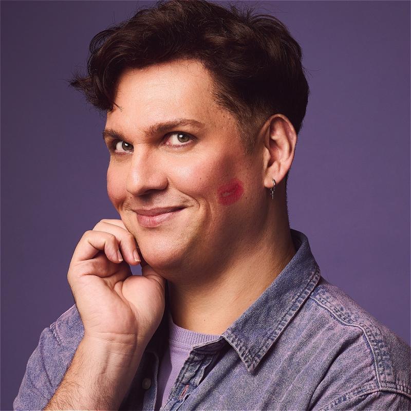 Photo of Dane looking cheekily at the viewe with a lipstick kiss on their cheek.