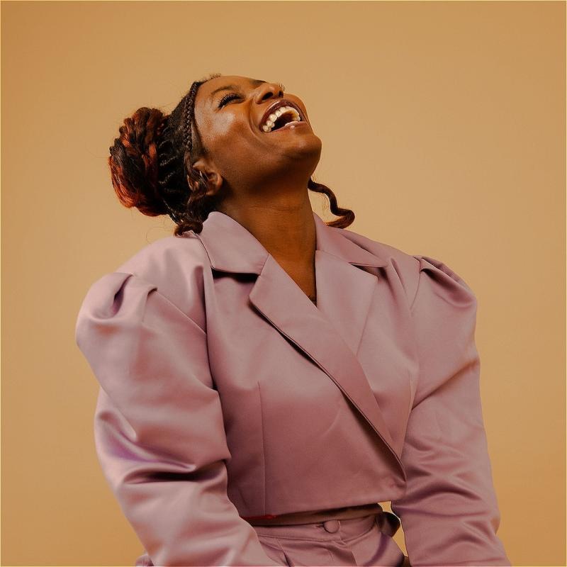 Sophie's head recoils back in laughter against a soft orange backdrop wearing a nice oversized coat