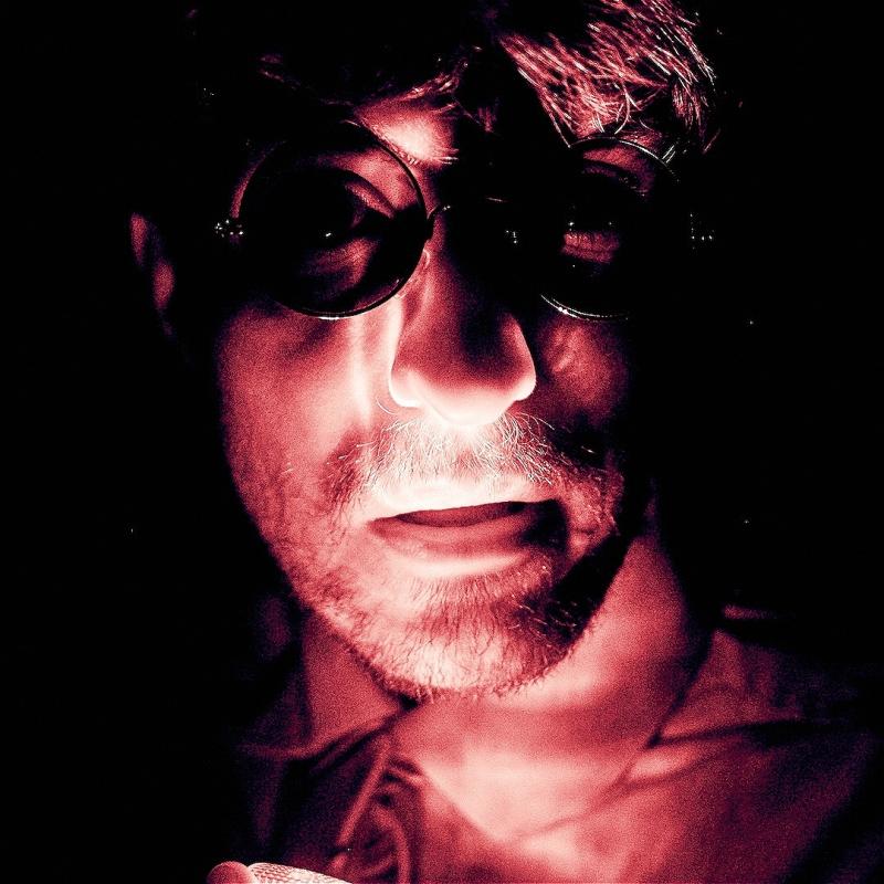 Close up of Joseph's face wearing circle rimmed glasses in stark edgy lighting looked befuzzled