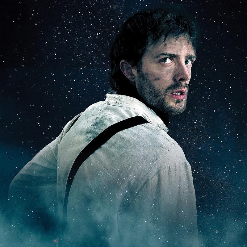 A dirty man stares over his shoulder, determined yet scared, before a sky full of stars.