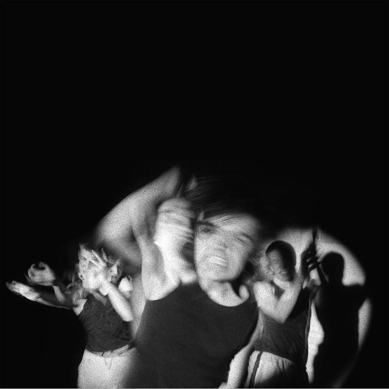 A black and white photo of three men blurred by their movements, before a black background.