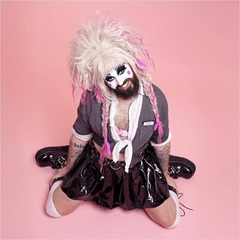 Baby Lame is kneeling on the floor in a very similar pose to the iconic Britney Spears album hit me baby one more time, but with significantly more makeup, more PVC, and bigger hair. Slay. 