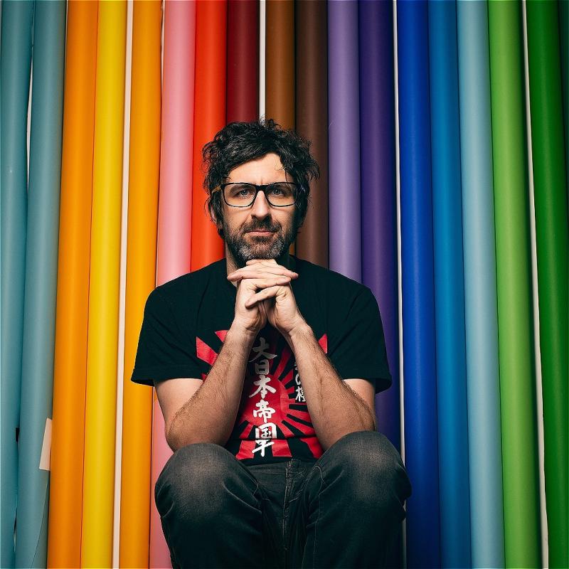 Mar Watson sits with his hands beneath his chin, wistfully staring ahead before a background of multi-colored pool noodles.