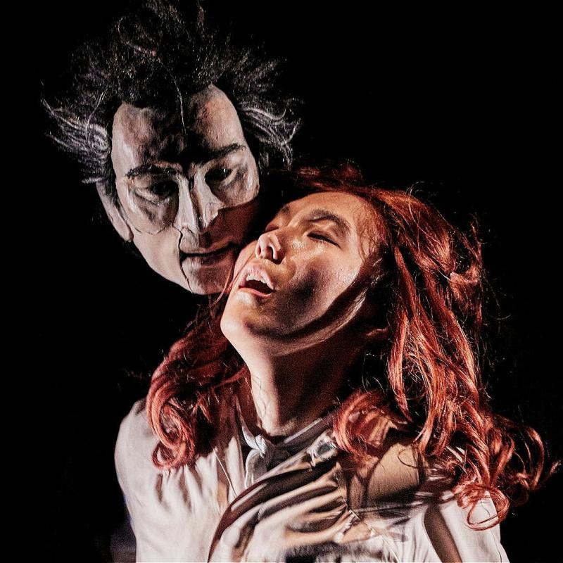 A man stares at a woman from behind as the woman looks up before a black background.