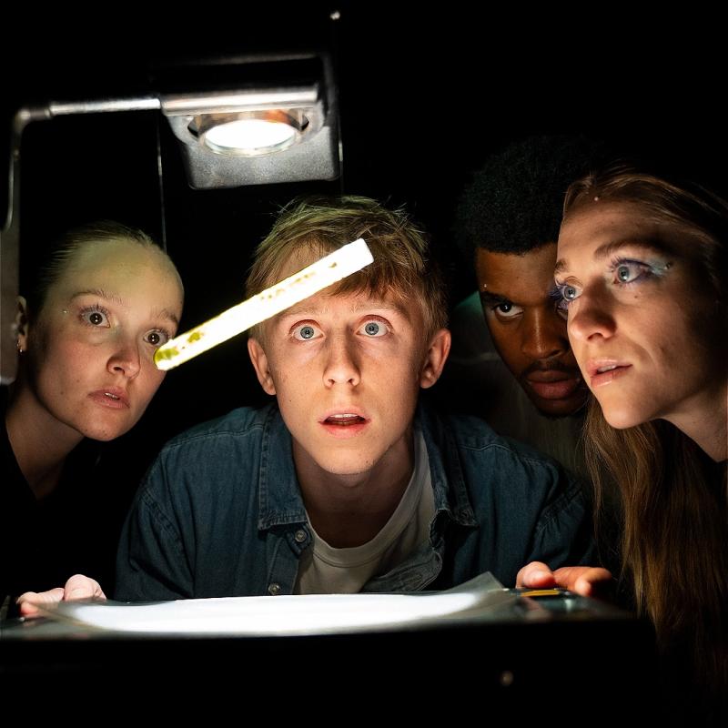Four people huddle around a test tube in the dark.
