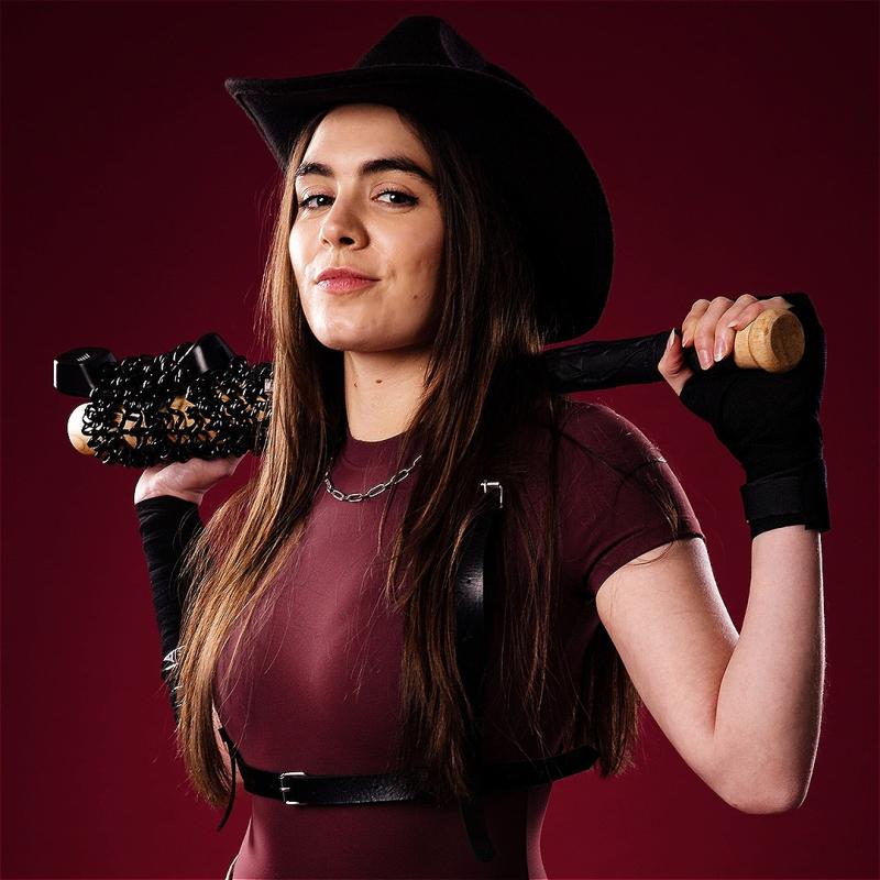 Amelia holds a baseball bat covered in barbed wire wearing a black leather harness and cowboy hat.