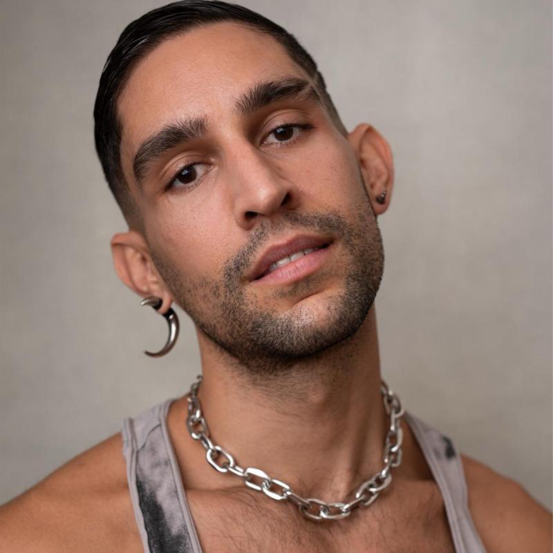 Headshot of Gigi with a large crescent moon shaped earring, chain necklace and a tank top.