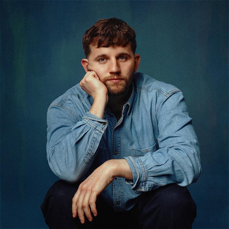 Rory looking into the camera in a blue denim shirt, with a blue background