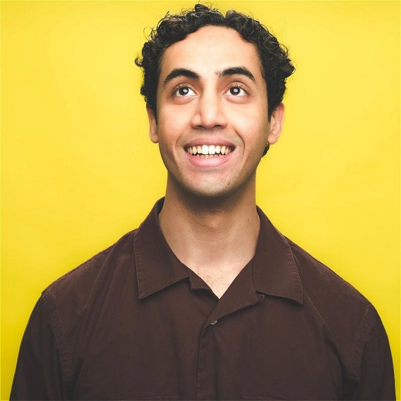 Omar is against a bright yellow backdrop, looking upwards and smiling 