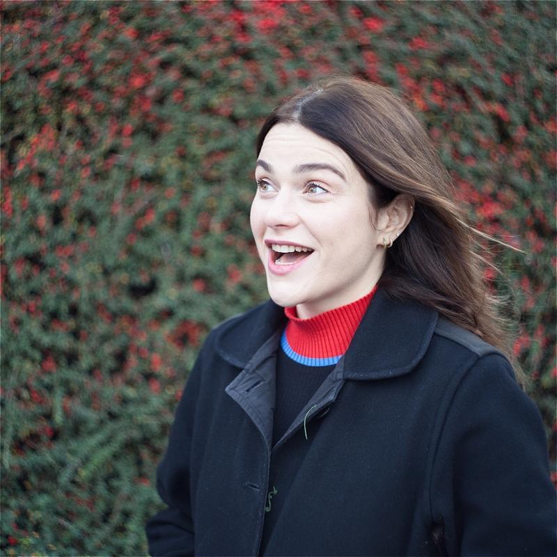 Davina stands outside, wearing a coat and a jumper with a red turtleneck