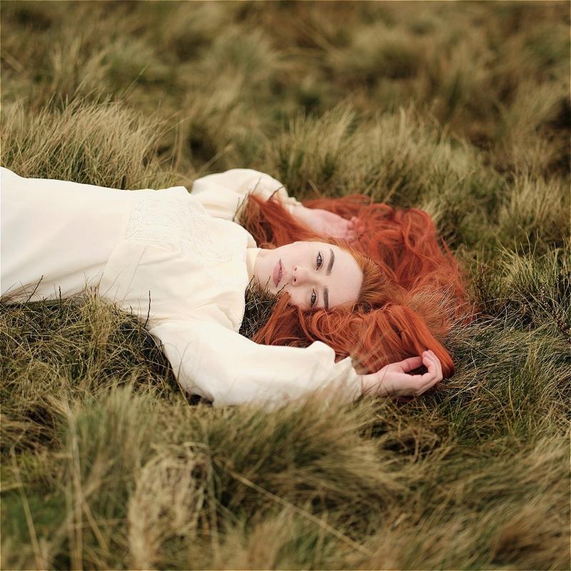Hannah, wearing a white linen dress, lying down in a field of grass. 