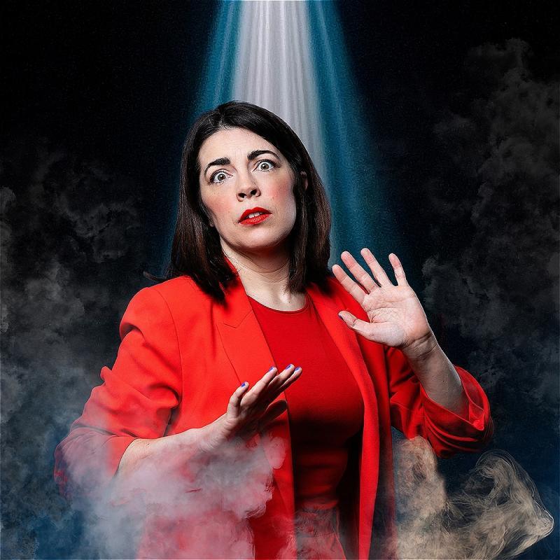 Rosie is wearing a red top and suit jacket, looking forward in fear. She is holding her hands up in defence and is surrounded by smoke. A beam of light shines down from above.