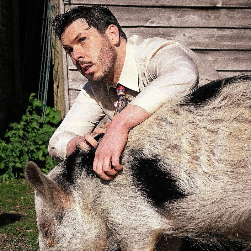 Dom crouched down behind a pig, wearing a white shirt and tie. 