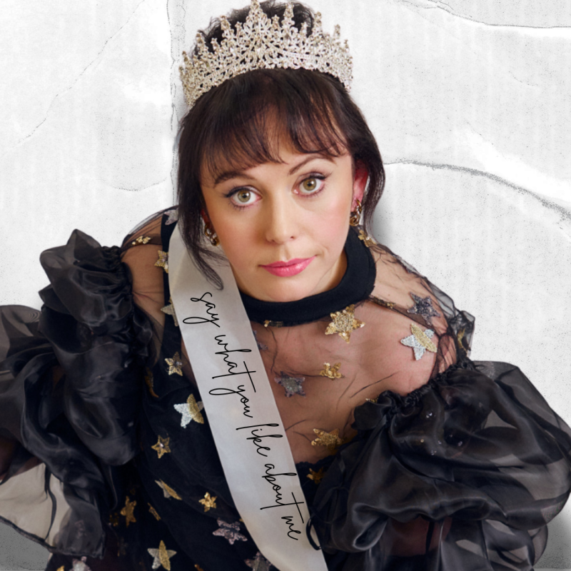 Amy looking up at the camera, wearing a tiara and a sash saying 'say what you like about me'. 