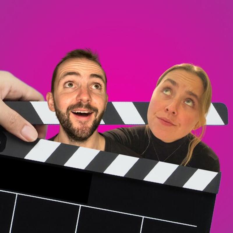 Two people with the heads between a film slate, looking up. They are against a pink background
