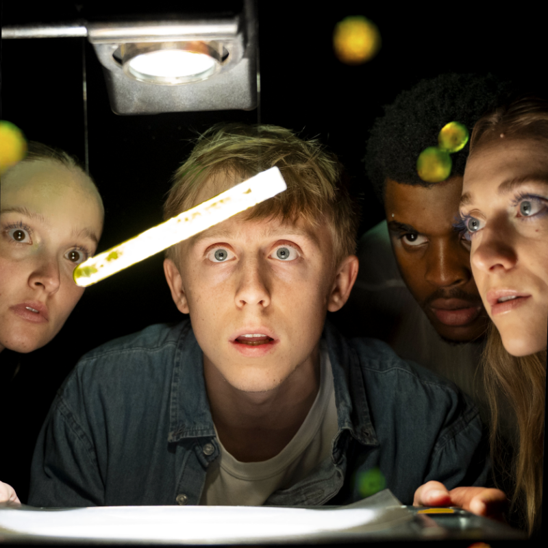 Four people huddle around a test tube in the dark.