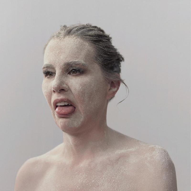 Kirsty has her hair pulled back and has white paint all over her face and bare shoulders, looking disgusted. 