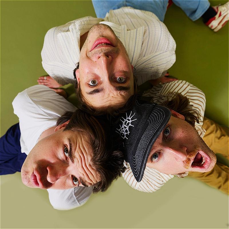 A bird's-eye picture of three white men sitting and looking up in surprise, the top of their heads touching each other.