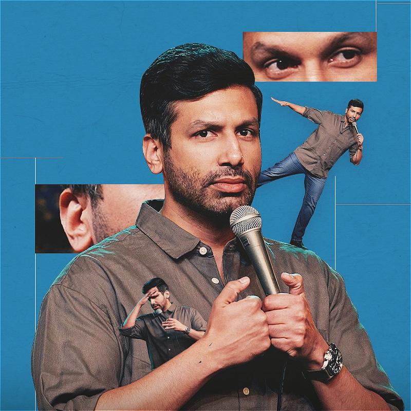 Kanan Gill, a brown Indian man with short black hair and beard and wearing a dark grey shirt and blue jeans, is holding a microphone and looking directly at the camera. On his shoulder is a smaller version of himself standing on one leg and arms out. Behind him are inserts of his eyes and ear on top of a blue background.