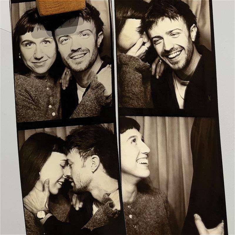 A heteronormative couple take photos in a black and white photobooth. They appear to be in love, and are laughing.