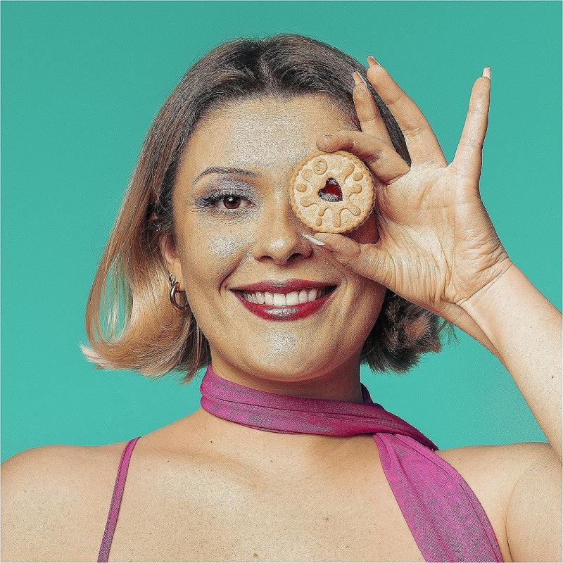 A woman with a bob smiles into the camera. She has a jammy dodger over one eye. 