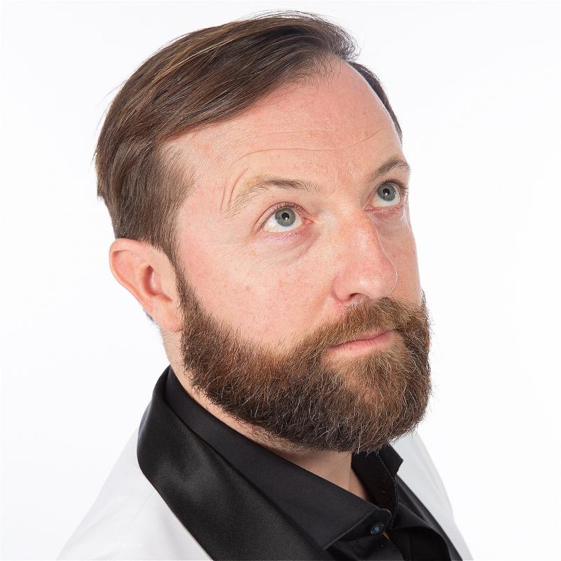 A man in a white suit jacket with black satin lapel, a beard, looks up to the ceiling.