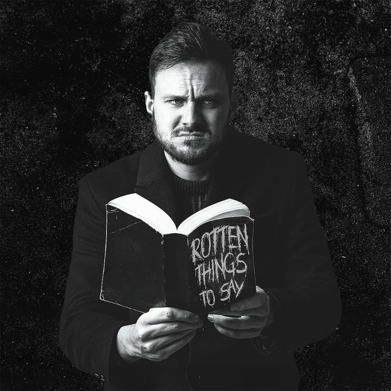 Black and white image of Mike grimacing while holding a book titled 'Rotten things to say'