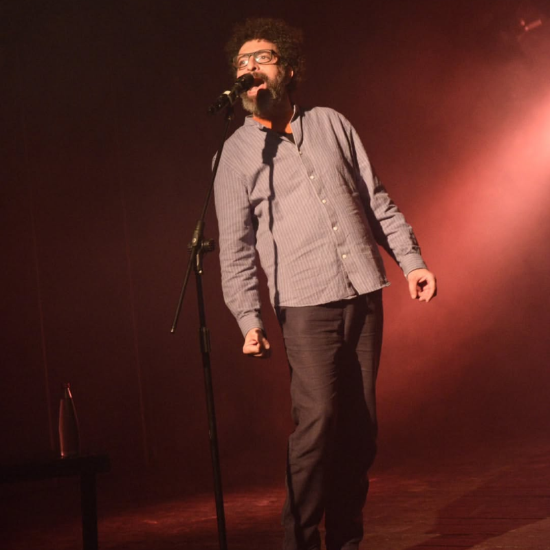 A performer, under the gaze of a harsh red lighting, passionately speaks into a microphone.