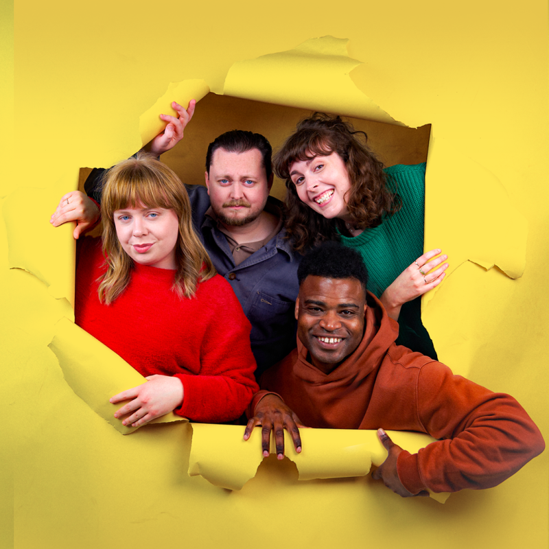 Four people peer through a yellow paper with torn edges.