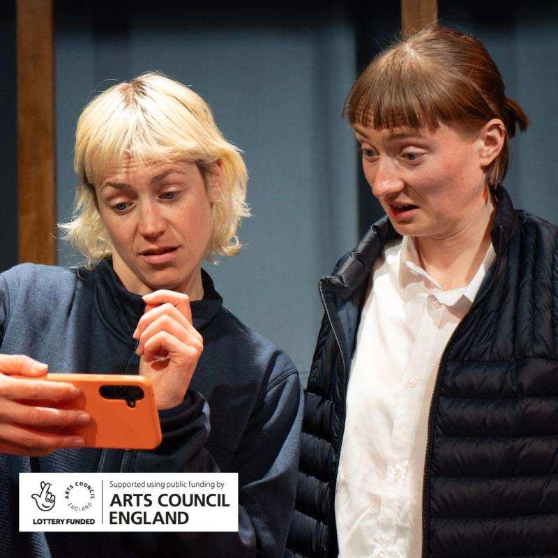 Two performers looking at a phone with a perplexed but intrigued expression on their face