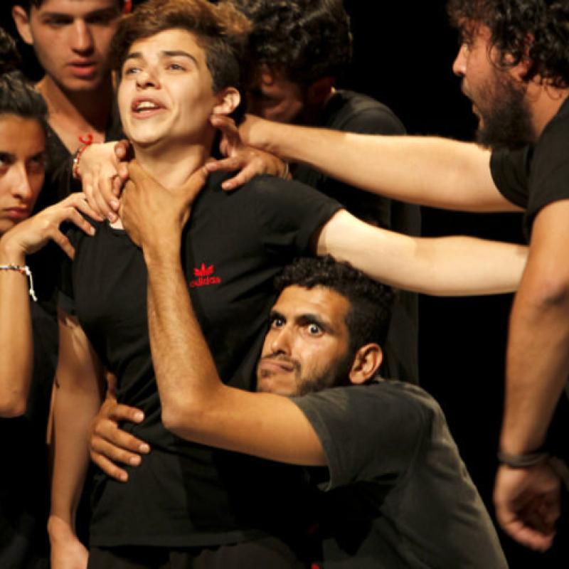 A group of performers engage is an intense stage tableau, with several people grabbing onto a central performer.