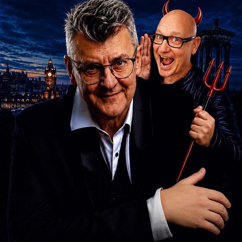 A person dressed in a suit smiles into the camera. Behind them as person dressed in devil horns and a mischievous expression looks as if they are mouthing something. London can be seen in the background. 