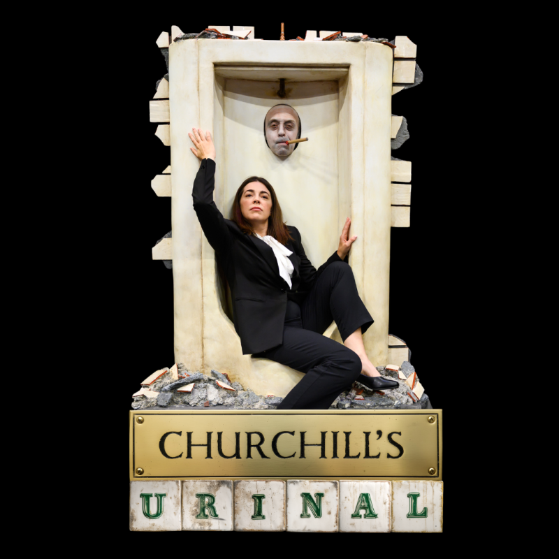 Woman wearing a suit crouch in a urinal with a man's face poking through the hole. The title of the show at the bottom.
