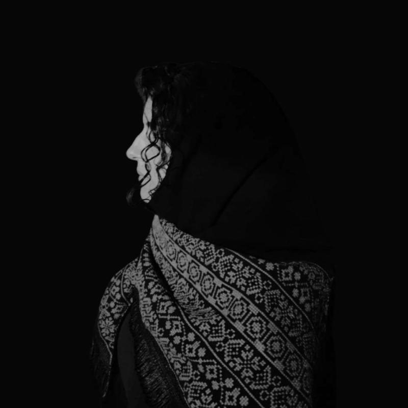 A black and white image of a woman's side portrait, with a traditional shawl on her shoulders