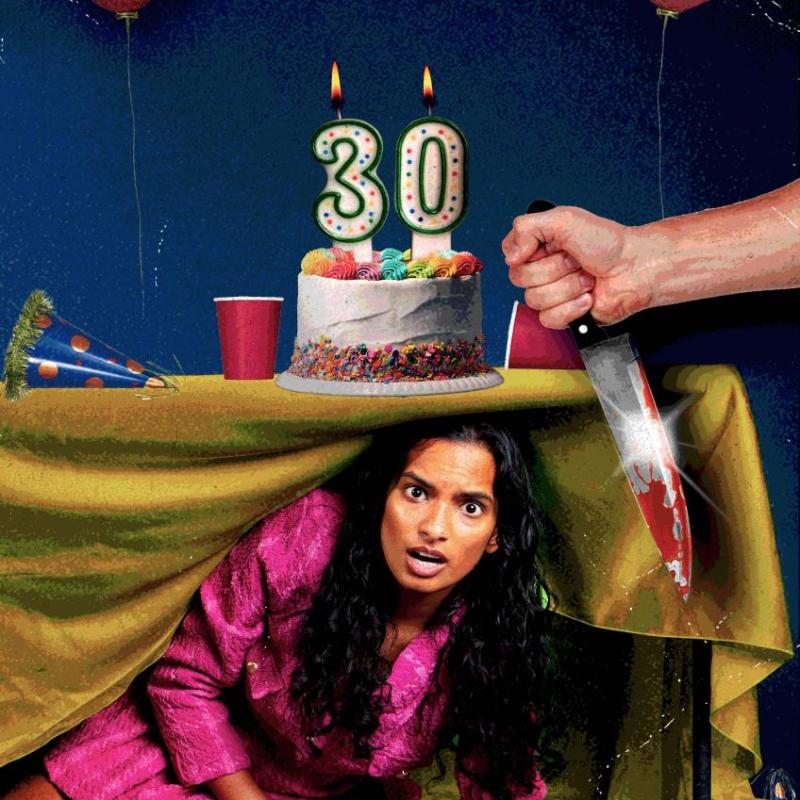 Abby hides under a table at a party. On the table there is a cake with '30' candles, and party cups and hats. In the foreground a hand reaches in from off-frame, holding a knife 